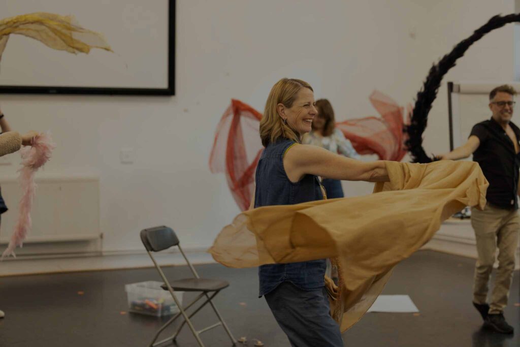 Leigh moving with sashs and feather boas in a group room, copyright Phil Tragen 2023