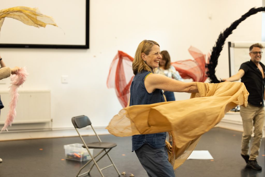 Leigh moving with sashs and feather boas in a group room, copyright Phil Tragen 2023