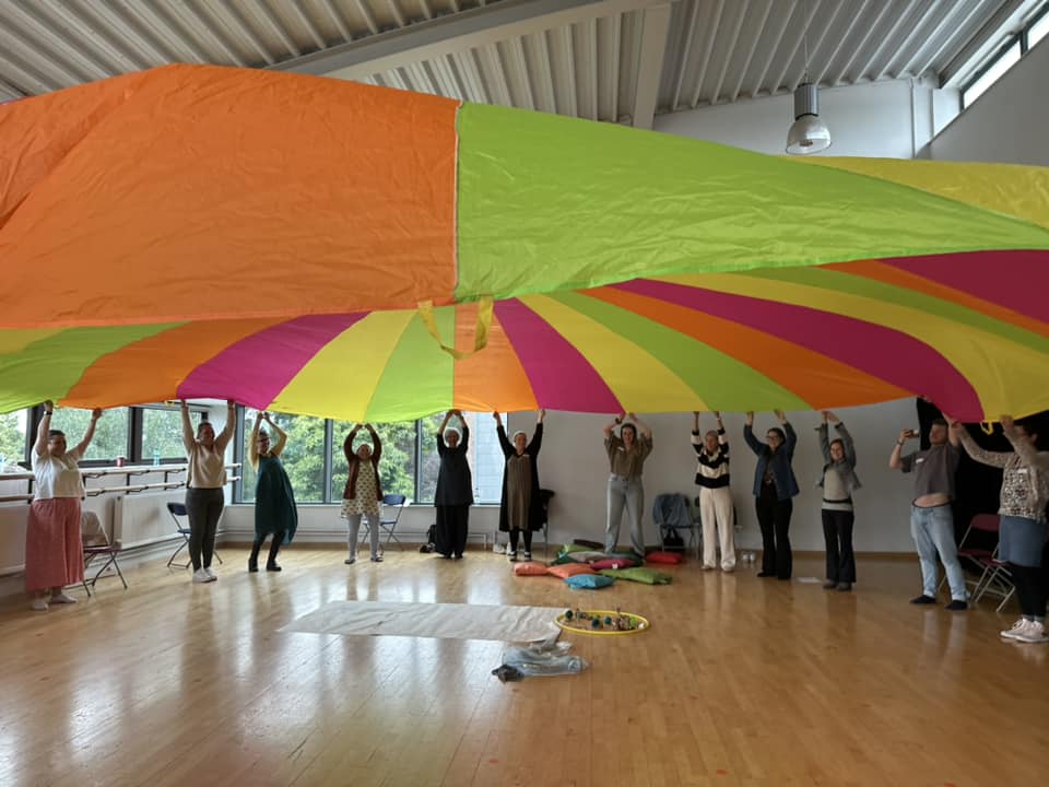 12 people holding up a multi coloured sheet