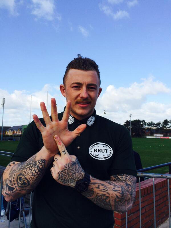 A rugby player performing the "one-in-five" hand gesture, with the index finger of one hand presented in front of the open palm of the other.
