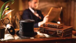 Table with a top hat, a stereoscope, some Victorian leather-bound books and a leather briefcase. A man reads a Victorian newspaper in the background.