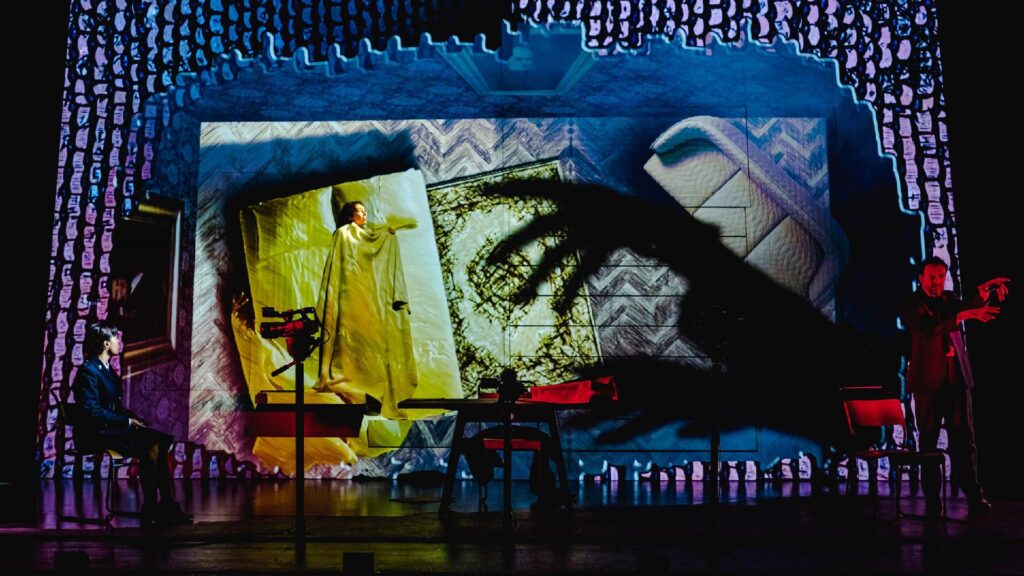Production photograph of Imitating the Dog’s 'Dracula: The Untold Story'. Is shows the shadow of a hand creeping across the stage towards an actress dressed in white.