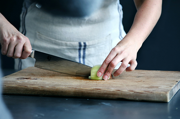 Photo by Caroline Attwood on Unsplash, cutting onions on a wooden chopping board
