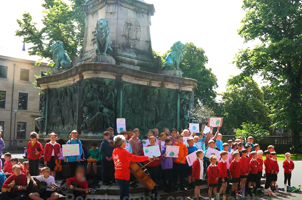 Bowerham Primary School children singing about climate change and the challenges  infront of a memorial