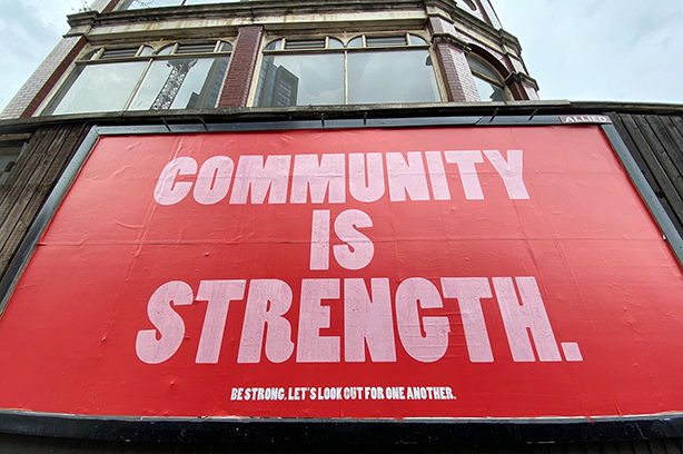 Photo by John Cameron on Unsplash. Community is Strength poster, large red and white public billboard saying 'community is strength'