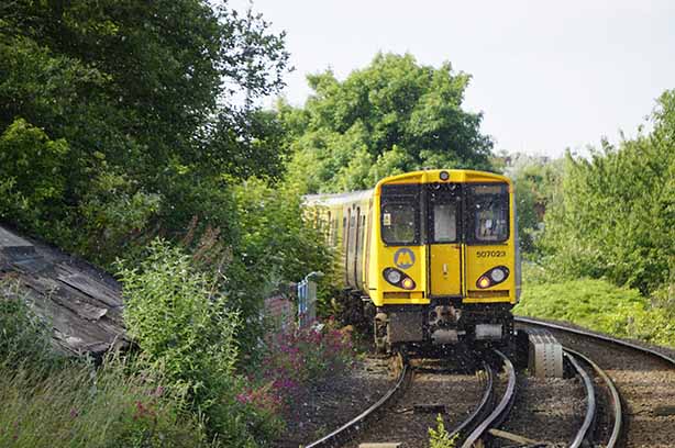 Photo by Sam on Unsplash, A Class 507 PEP departs Bootle New Strand railway station on its way to Southport, with a flurry of petals in its wake