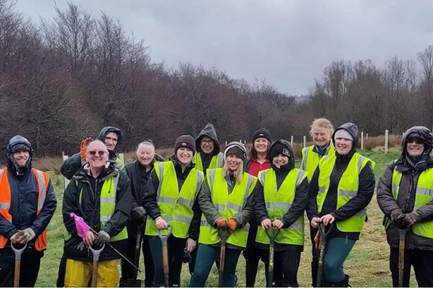 A group of people from Hyndburn Proffitts CIC Community Projects standing in hi-viz holding spades after planting trees