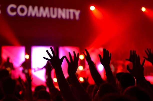 A crow of people at a gig with their hands in the air watching a band, light up with a backdrop of red light