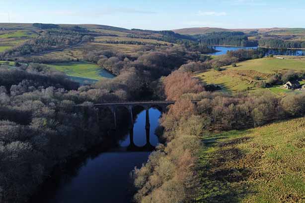 Railway line across a bridge over a river, surrounded by trees and fields