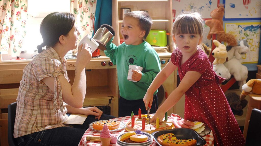 Two nursery students and a teacher in a play kitchen