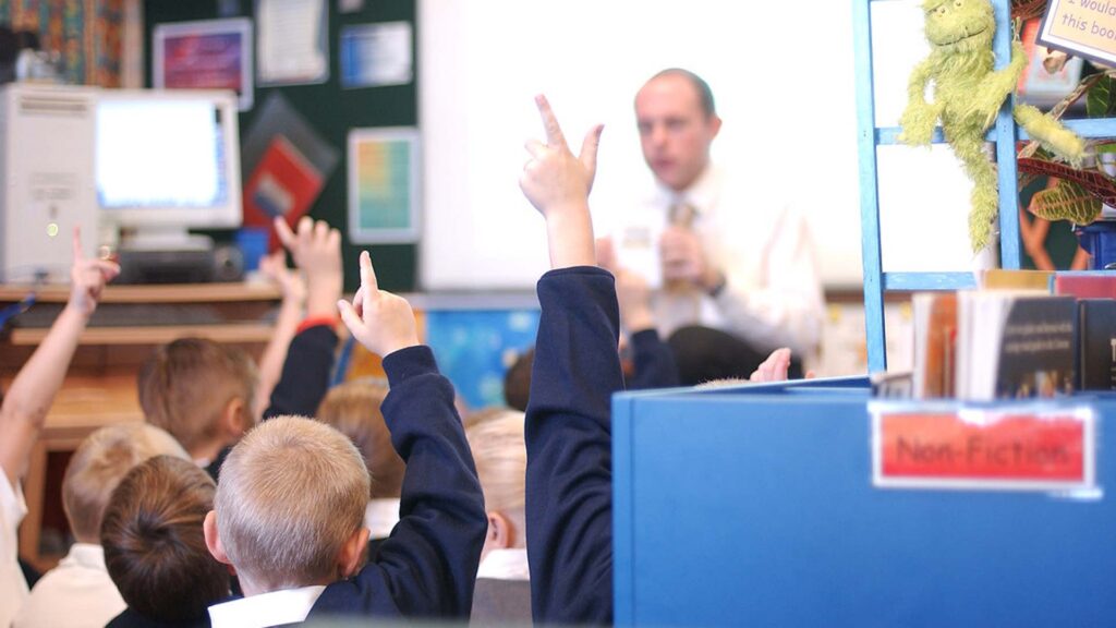Primary school students put their hands up to answer a question during an English class