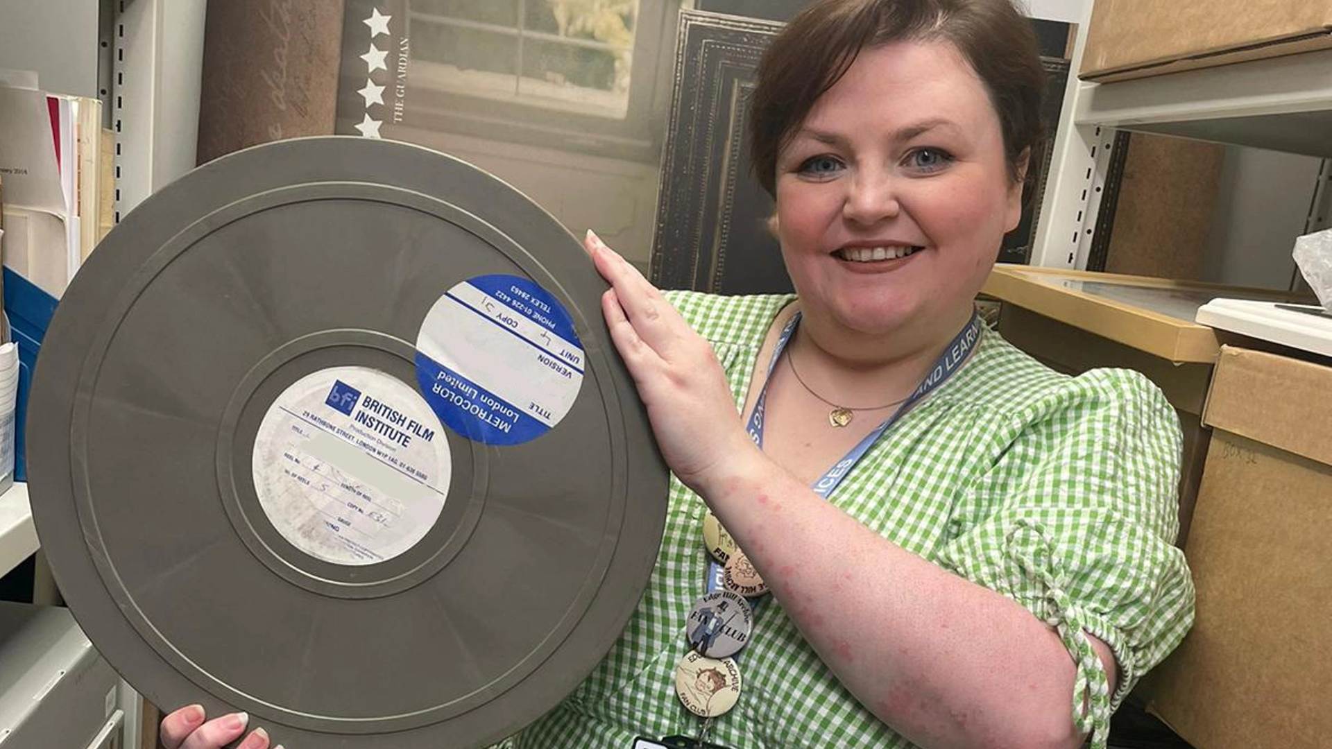 Sophie Smith wearing a green dress holding an archive reel and smiling at the camera 