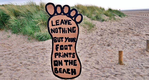 Beach dunes with a wooden footprint sign stating 'leave nothing but foot prints'