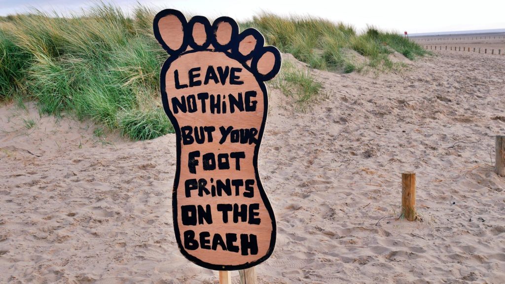 Beach dunes with a wooden footprint sign stating 'leave nothing but foot prints'