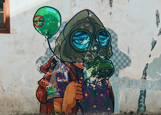 Graffiti on wall depicting a person holding a green balloon wearing a gas mask