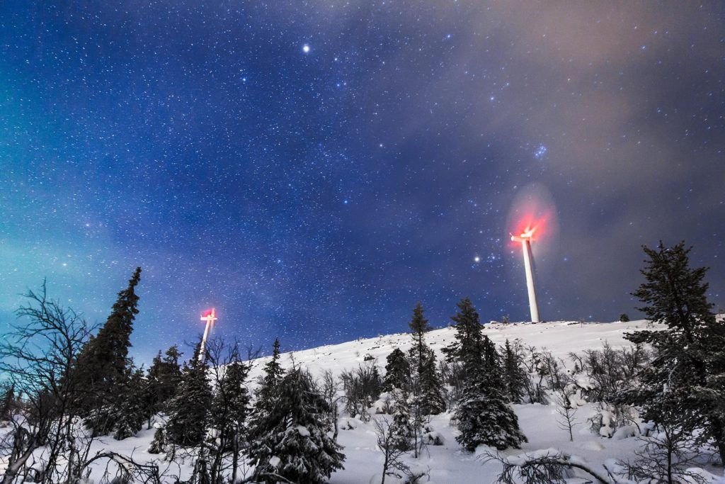 Two wind turbines and night on top of a snowy forested hill