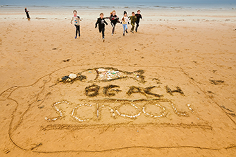 Kids running together along the beach in front of words 'beach school' written in the sand