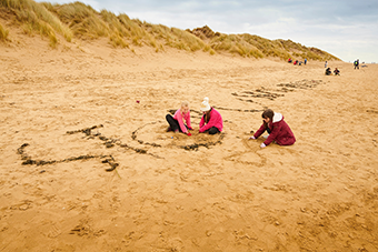 Kids together on the beach writing words 'beach school' in the sand