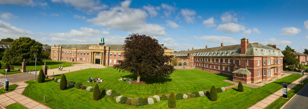 Image of the main building at Edge Hill University. Students sitting on the grass at the front.