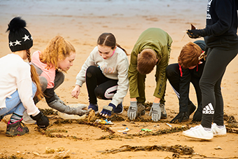 Kids together on the beach writing words 'beach school' in the sand
