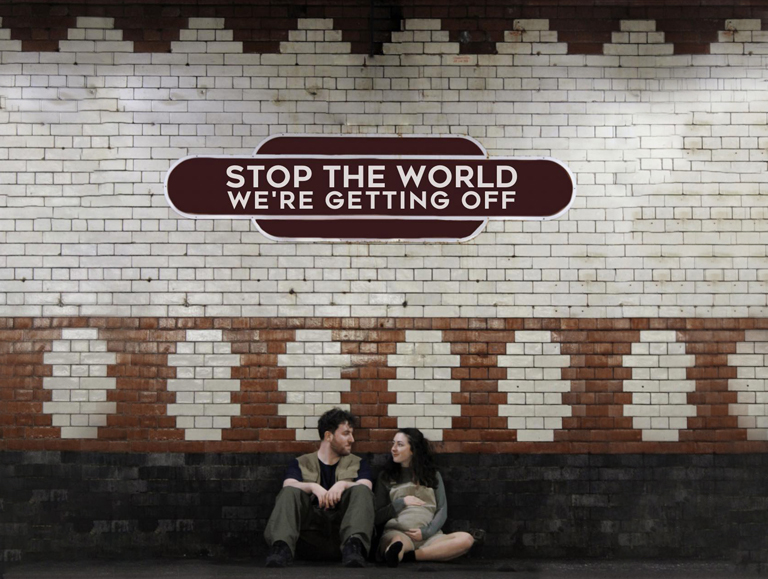 Man and a pregnant woman sitting on the floor in an old train station with tiled walls