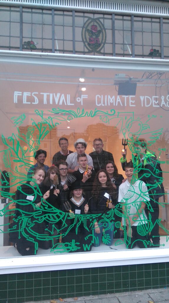 Future Coast Youth Project, students in the window of a shop all holding up garden tools.