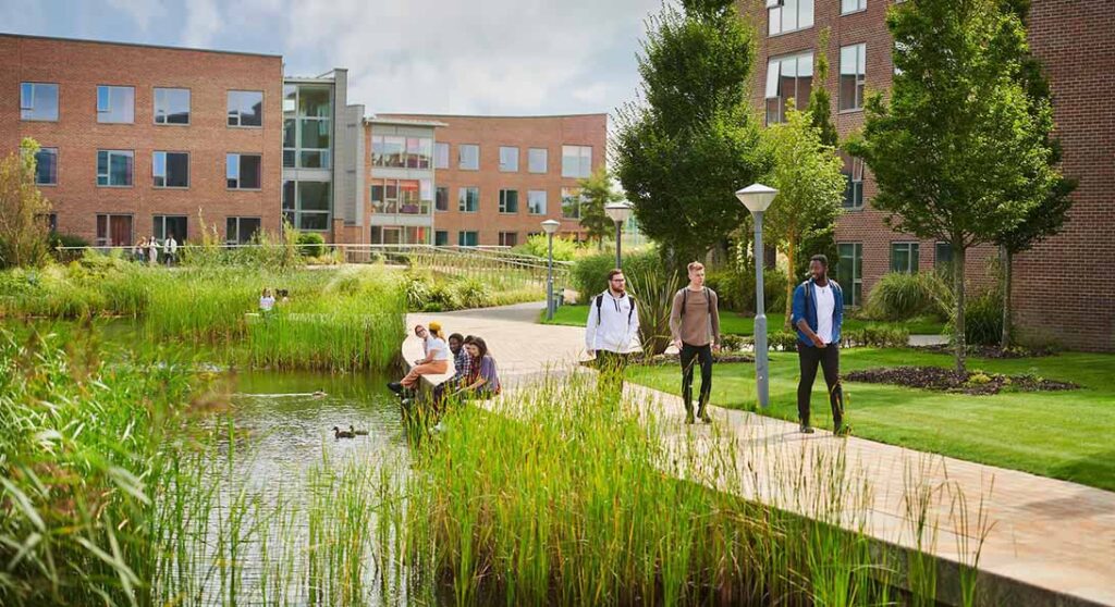 Students walking past the Chancellors accommodation building and students sitting by the lake.
