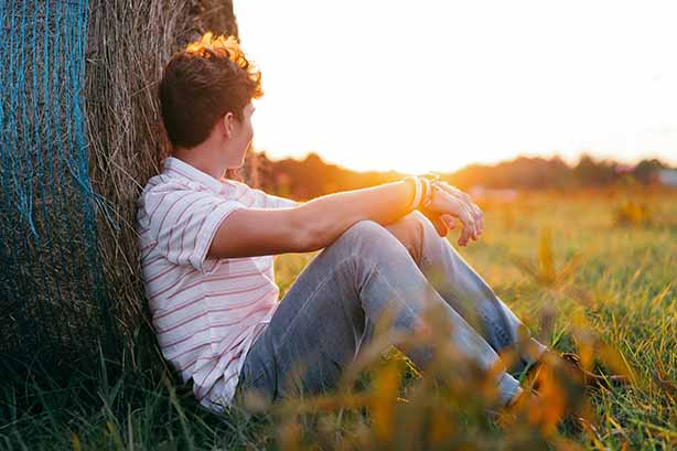 Photo by Davis Evans on Unsplash, man sitting against a hay bail watching the sun rise