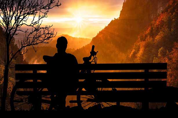 Man sitting on a bench watching the sunset with his bike resting behind